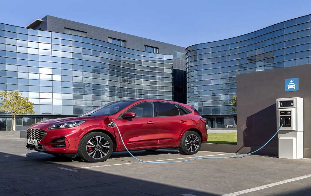 Elektro Ford Kuga auf einem Parkplatz mit Bürogebäuden im Hintergrund