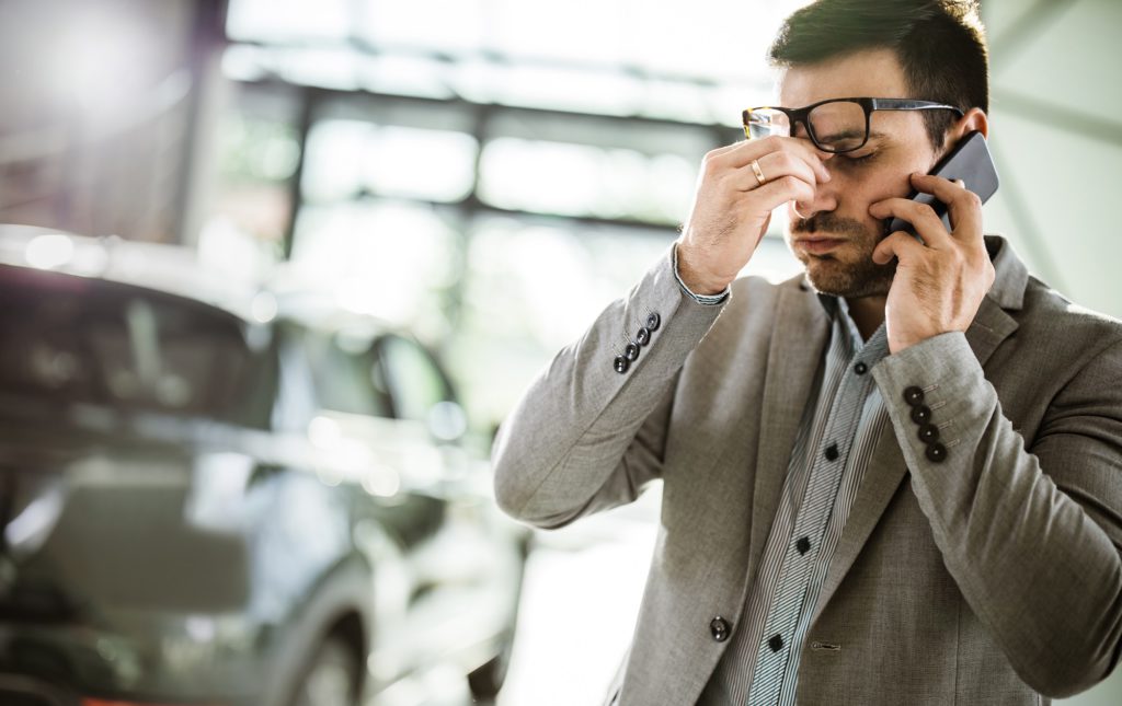 Geschäftsmann hat Kopfschmerzen, während er auf dem Handy in einem Auto-Showroom spricht